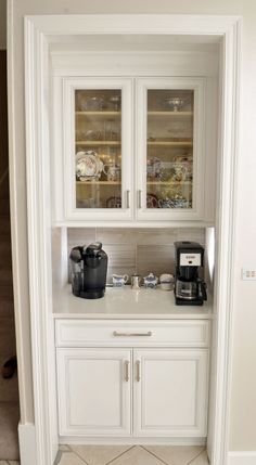 a white cabinet with two glass doors and some dishes on it's shelves in a kitchen