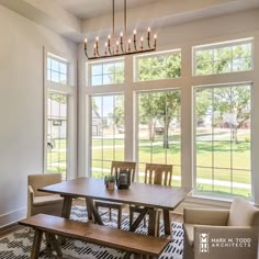 a dining room table and bench in front of large windows with lots of natural light