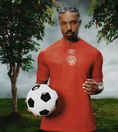 a man holding a soccer ball in front of a tree