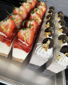 several desserts are arranged on trays with gold leaf decorations and strawberries in the middle