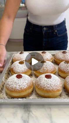 a woman standing in front of a tray filled with donuts covered in powdered sugar