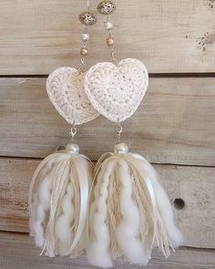 two white heart shaped beads hanging from a chain on a wooden wall with pearls and chains