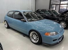 a blue car parked in a garage next to two other cars with their hoods open