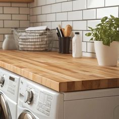 a wooden counter top in a kitchen next to a washer and dryer with a potted plant on it