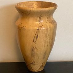 a large wooden vase sitting on top of a black table next to a white wall