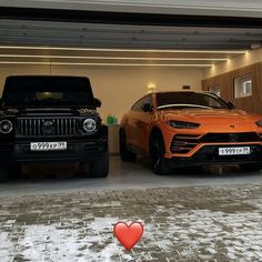 two cars are parked in a garage with snow on the ground and one is orange