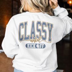 a woman wearing a white sweatshirt that says classy and kick off on the back