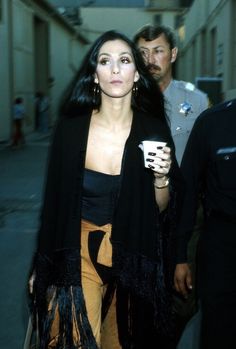 a woman walking down the street with a cup in her hand and two men standing behind her