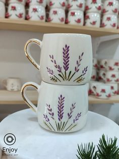 two coffee cups are stacked on top of each other with purple flowers painted on them