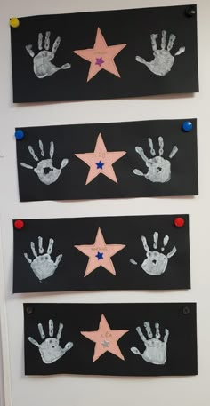 three handprints on black paper with pink and blue stars hanging from the wall