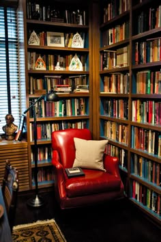 a red chair sitting in front of a bookshelf filled with lots of books