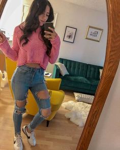 a woman in ripped jeans taking a selfie with her cell phone while standing in front of a mirror