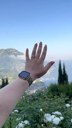 a woman's hand with a watch on her wrist in front of flowers and mountains