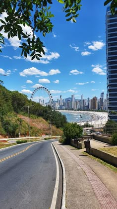 an empty street next to the ocean with a ferris wheel in the distance and a city skyline behind it