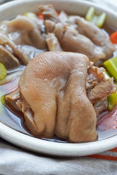 a white bowl filled with meat and vegetables on top of a cloth covered tablecloth