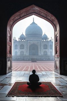 a person sitting on a rug in front of an archway with a building in the background