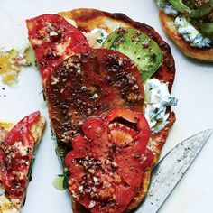 two slices of pizza with tomatoes, cheese and broccoli on them next to a knife