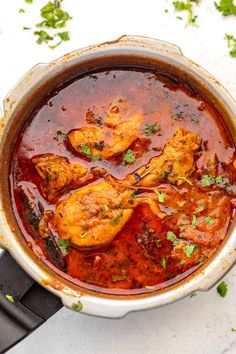 a pot filled with chicken curry and garnished with cilantro on the side