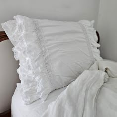 a bed with white linens and ruffled pillow cases on it's headboard