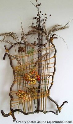 a sculpture made out of branches and twigs with berries on them, sitting against a white wall