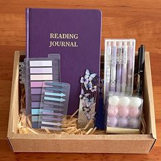 a purple book sitting on top of a wooden table next to pens and pencils