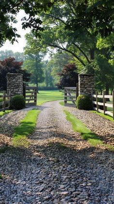 a gravel driveway leading to a gated in area with trees and grass on both sides