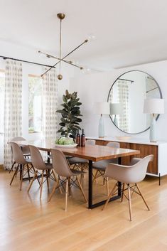 a dining room table with chairs and a round mirror on the wall in front of it