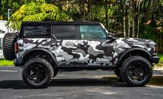 a camouflage jeep parked on the street in front of some trees and bushes with no one around it