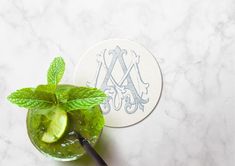 a mojito with limes and mint on a marble counter top next to a monogrammed coaster