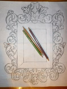 two pencils sitting on top of a piece of paper next to an ornate frame