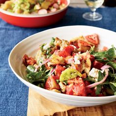 a white bowl filled with salad on top of a wooden cutting board next to a glass of wine