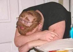 a man with glasses leaning his head on a desk