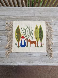 a handmade rug with animals and trees on it sitting on a bench in front of a wooden slatted fence