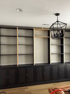 a living room with black bookcases and wood flooring on the walls, along with a chandelier hanging from the ceiling