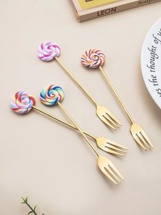 three forks and four lollipops sitting on top of a table next to a plate