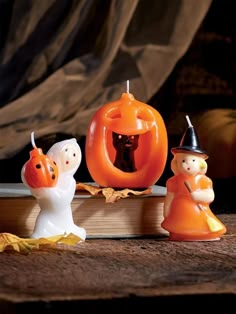 three halloween figurines sitting on top of an open book with pumpkins in the background