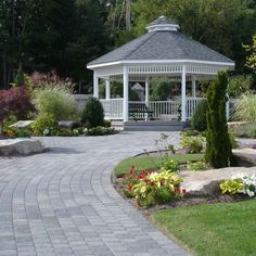 a white gazebo sitting in the middle of a park surrounded by flowers and trees