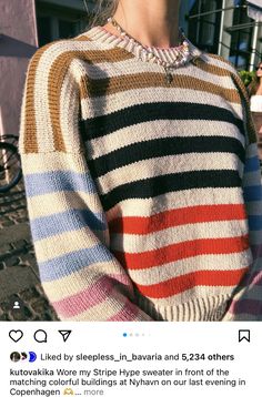 a woman standing in front of a building wearing a multicolored sweater and sunglasses