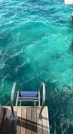 a chair sitting on top of a wooden dock next to the ocean with clear blue water