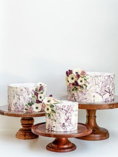 three cakes with flowers on them sitting on wooden pedestals