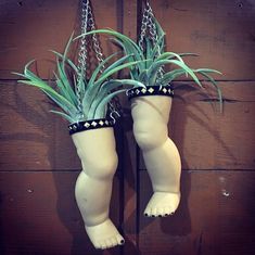 two white ceramic planters with plants in them hanging from chains on a wooden wall