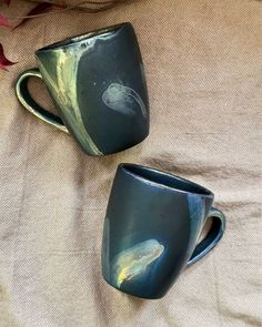 two coffee mugs sitting on top of a bed next to each other, one is green and the other is blue