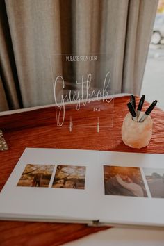 an open book sitting on top of a wooden table next to pictures and pen holders