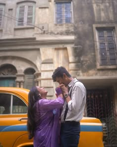 a man and woman standing next to each other in front of a yellow car on the street