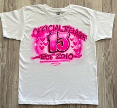 a white t - shirt with pink spray paint on it that says official teenager 13th birthday