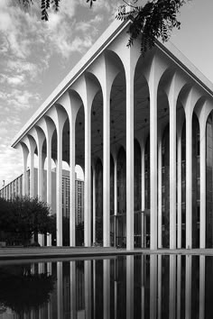 a black and white photo of a building with columns on the side, reflecting in water