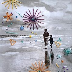 two people are walking on the beach with colorful objects in the sky above them and an overcast sky behind them