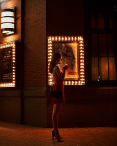 a woman standing in front of a building at night looking at her cell phone while wearing high heels