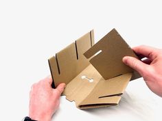 two hands are opening up a cardboard box with the lid open and one hand is holding it