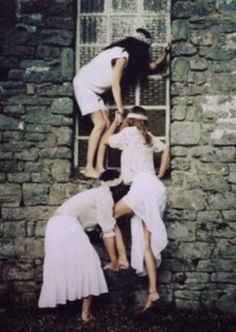 three women in white dresses climbing up the side of a stone building